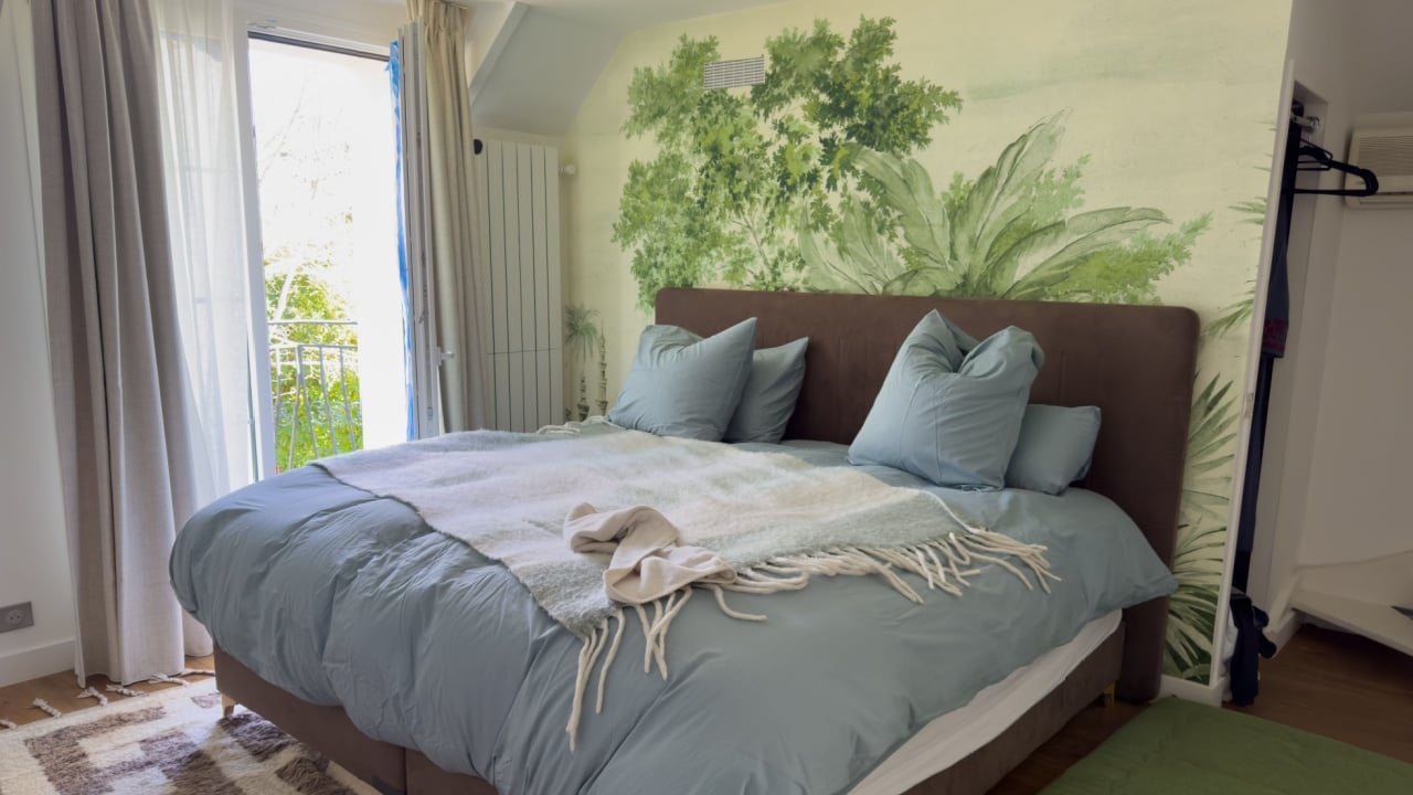 A stylish bedroom features a lush green mural that evokes nature, complemented by a soft blue bedspread and elegant pillows, perfect for relaxation and comfort.