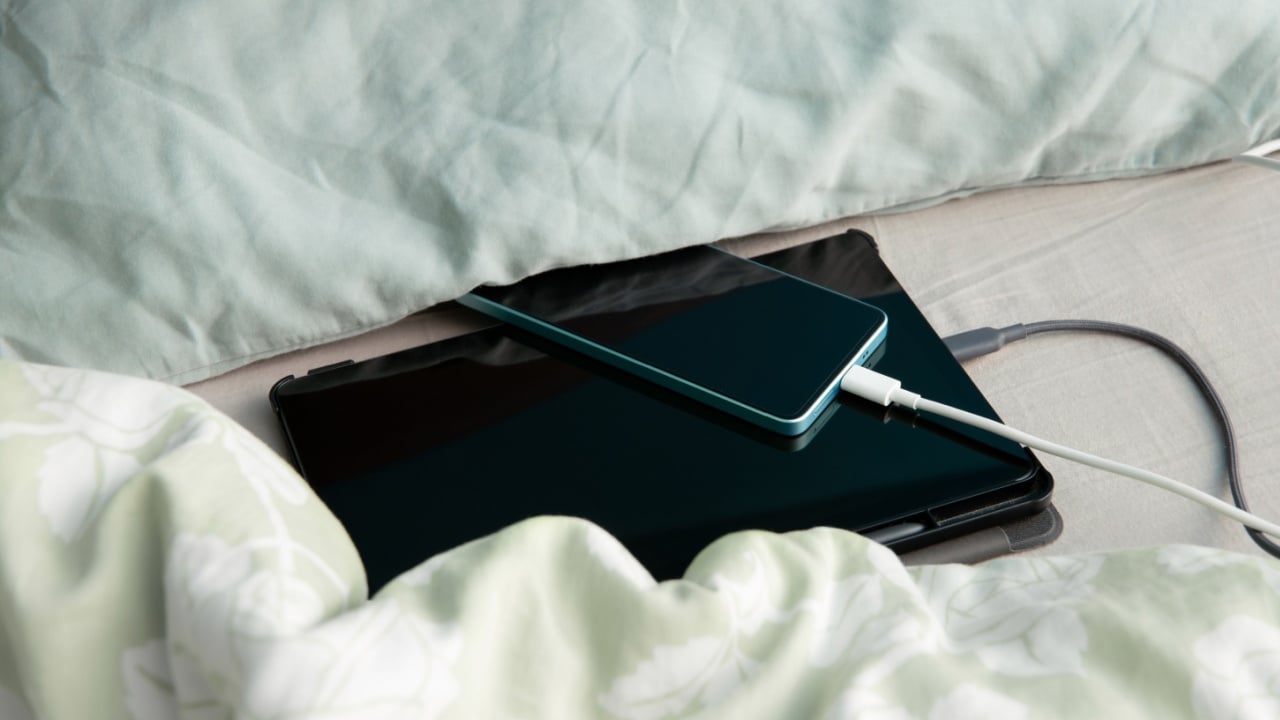 Smartphone and tablet computer are charging in bed under a pillow and blanket. Concept of overheat and fire hazard.