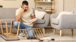 Thoughtful young man with manual and screwdriver assembling bench at home
