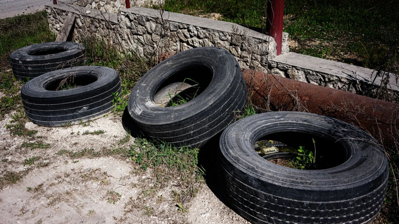Four old tires lying on the ground next to a stone wall and grass