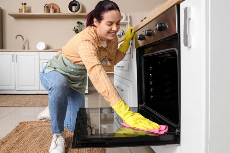 Young woman cleaning oven in kitchen
