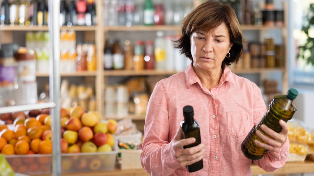 Uncertain mature female buyer choosing some olive oil in grocery store
