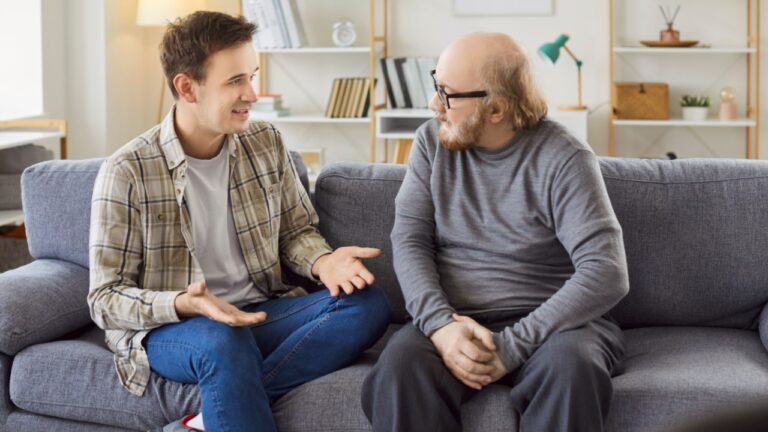 Adult son and a senior father talking. Old man in his 60s sitting on the couch together with his grown up son and listening to him ready to share his life wisdom. Parents and children concept