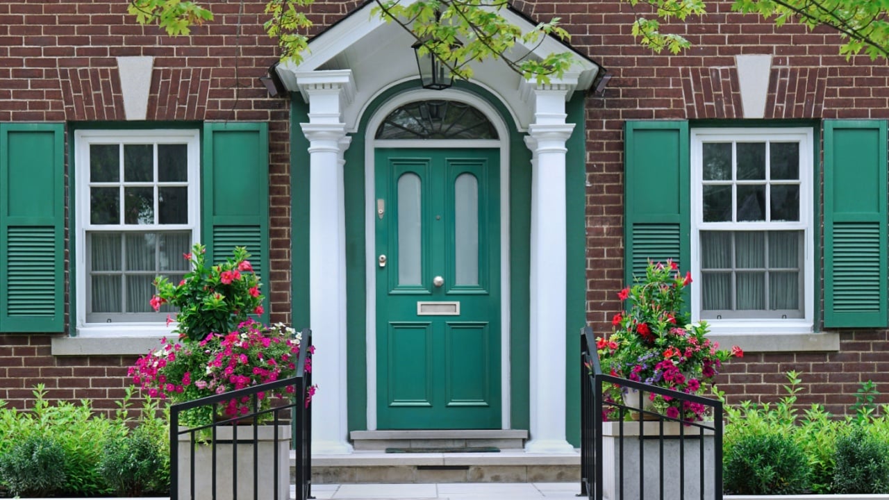 Front door of brick home with shutters and flower pot