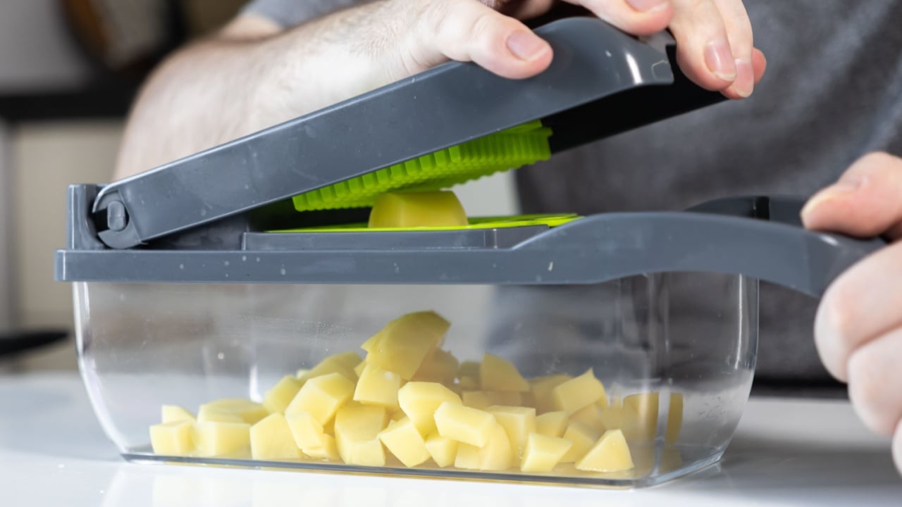 Close-up of hands using a modern transparent vegetable chopper, cubing fresh potatoes for convenient, healthy meal preparation in a contemporary kitchen setting