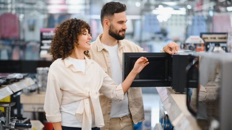 Young couple selecting a new microwave oven in a home appliance store, examining features and making a purchasing decision