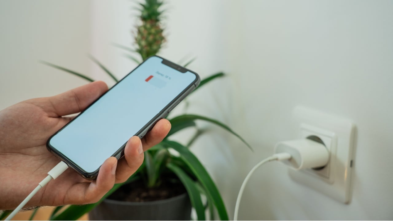 Close-up of a smartphone connected to a wall socket with a USB cable for charging. Modern technology and home electricity concept.