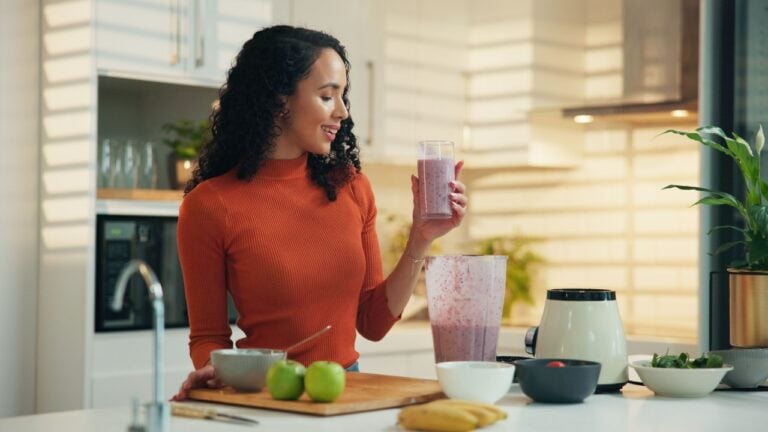 Woman, blender and happy with glass in kitchen for healthy drink, diet and supplement for detox at home. Person, machine and smile for benefits, nutrition or gut health with wellness at apartment