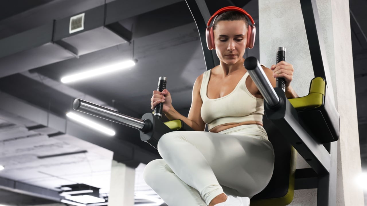 Athletic woman in headphones training on power tower in gym, low angle view.