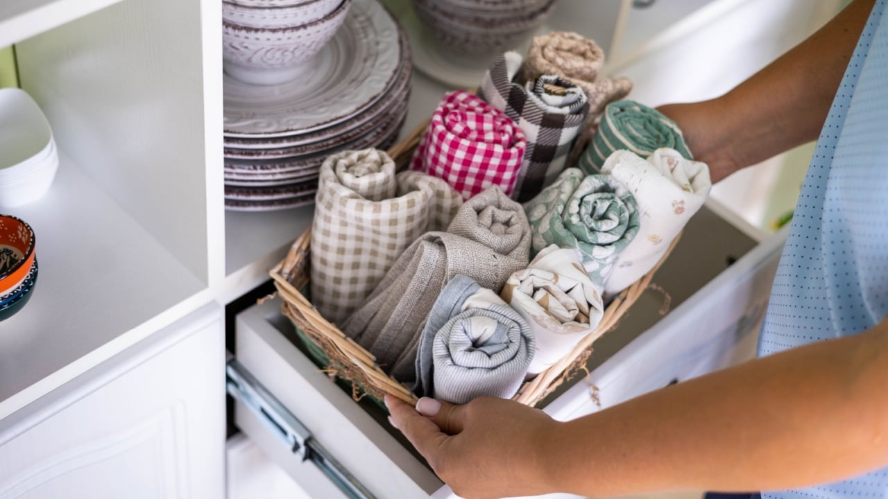 Woman placing kitchen textile towel roll in whicked basket shelf rustic retro commode top view