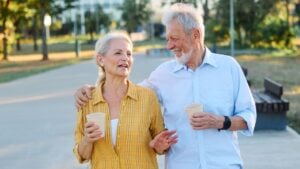 Happy active senior couple having fun talking drinking coffee and bonding in park outdoors