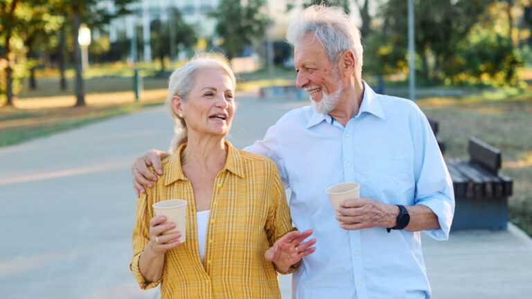 Happy active senior couple having fun talking drinking coffee and bonding in park outdoors