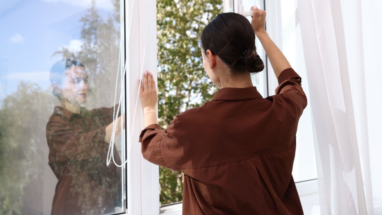 Woman opening modern window at home, back view