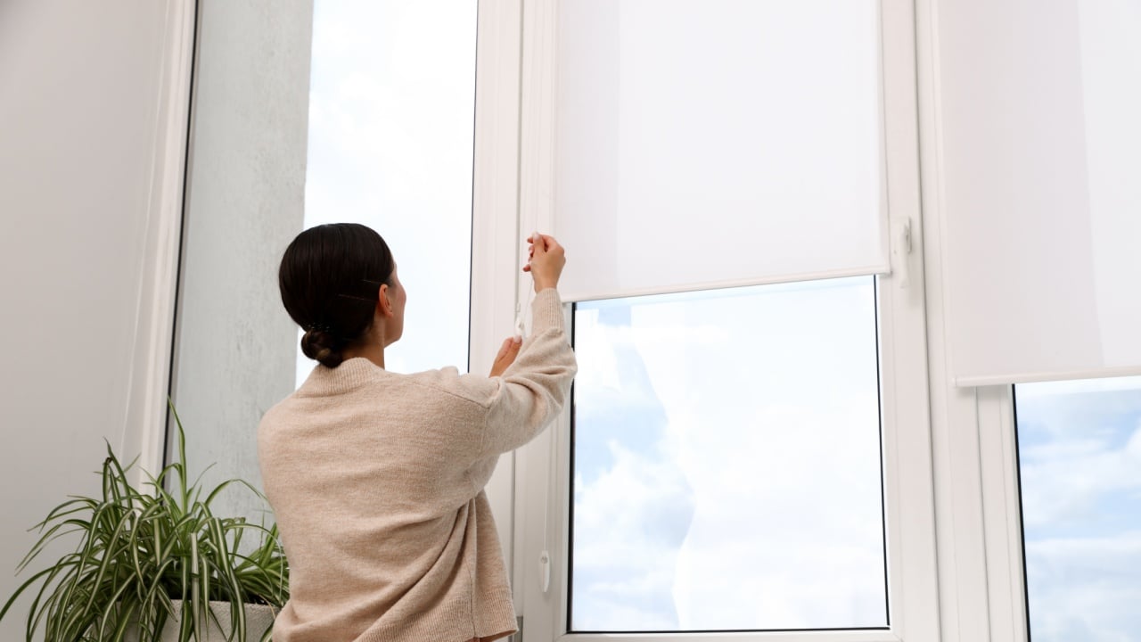 Woman opening roller blinds on window indoors