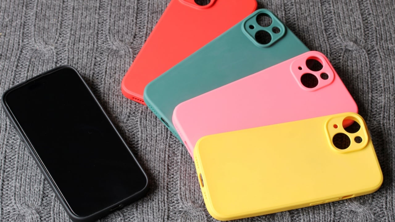 Mobile phone laying next to various colored smartphone cases on gray knitted background