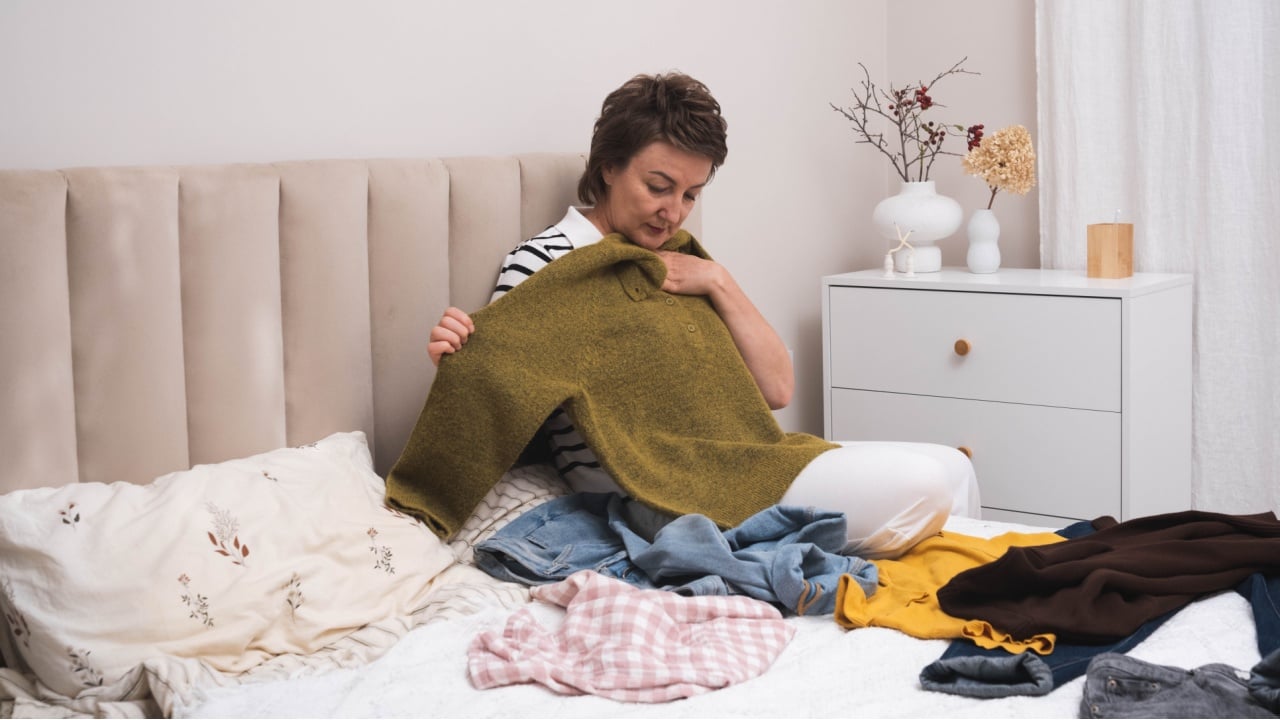 Woman selecting clothes from her wardrobe for donating to a Charity shop. Decluttering, Sorting clothes and Cleaning Up. Reuse, second-hand concept. Conscious consumer.