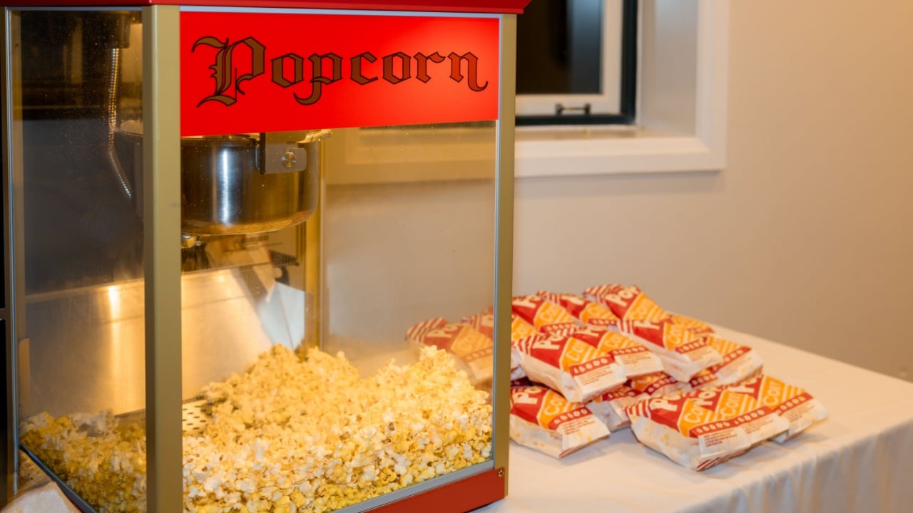 A bright red popcorn machine filled with freshly popped corn sits beside a neatly stacked pile of popcorn bags - the perfect touch of fun and nostalgia for any celebration