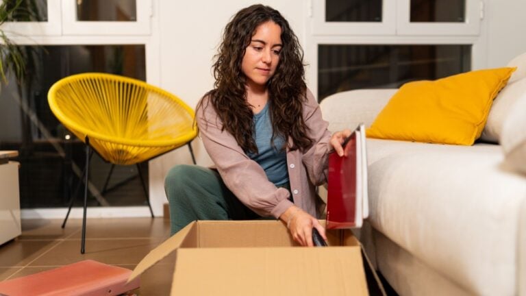 Woman organizing her belongings, putting documents and books into a moving box in her living room