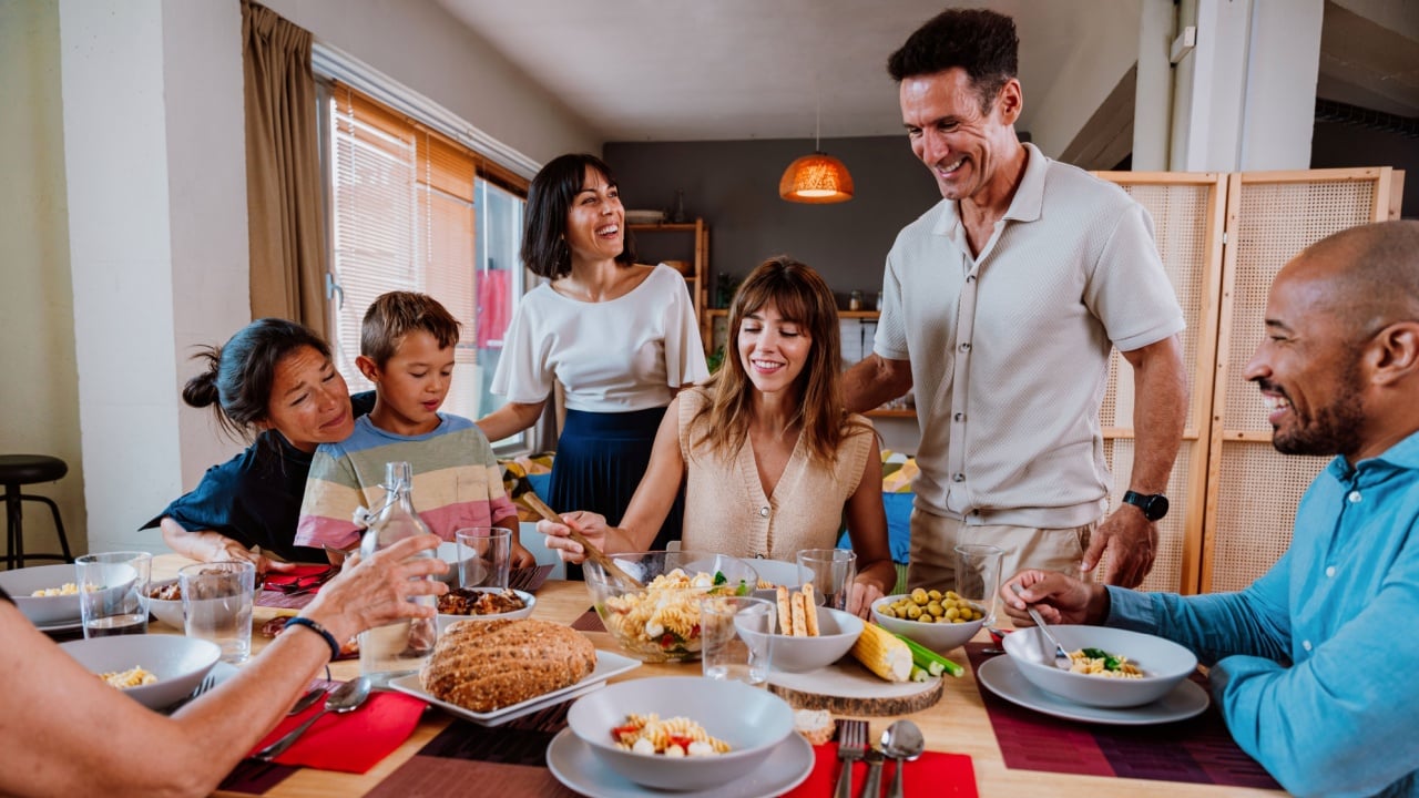 Family and friends reunion at home. Happy multigenerational, diverse family sharing a joyful, casual dinner at home — laughing, eating, and bonding around the table