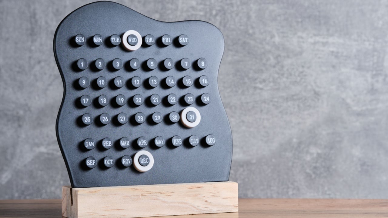 Modern black perpetual calendar on wooden base stands against gray wall, with markers highlighting Wednesday and December 31