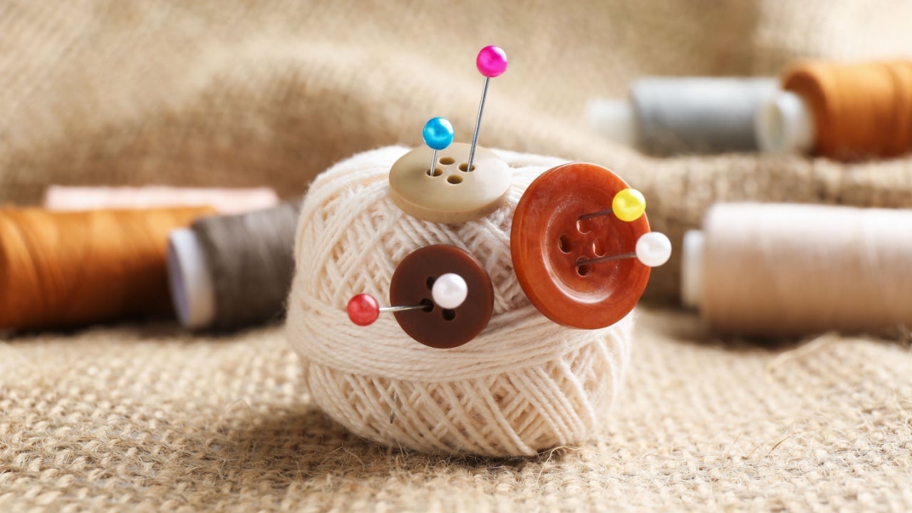 White yarn with pins, buttons and spools of threads on burlap cloth, closeup