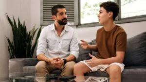 Father listening attentively to his teenage son during a calm conversation at home. Concept of active listening, emotional intelligence and family communication