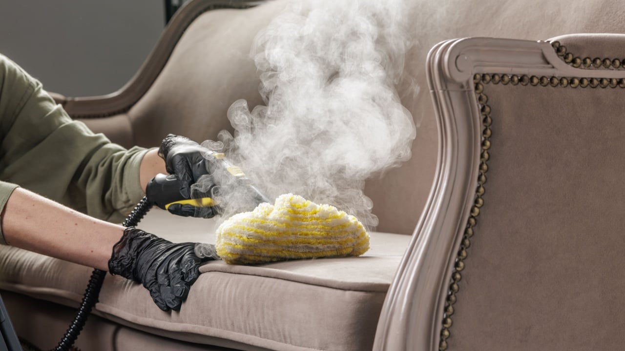 Gloved cleaner uses a steam tool with microfiber pad to deep clean sofa cushion and remove stains, ideal for a cleaning service website banner or advertising.