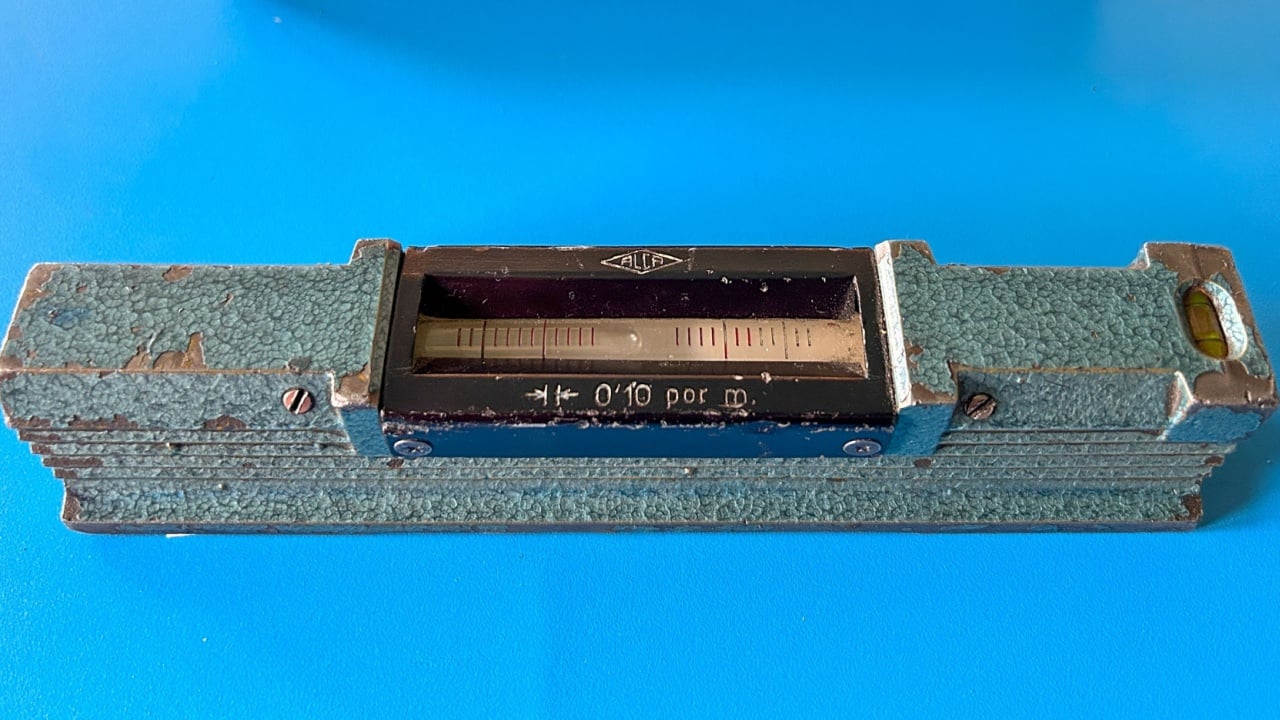 Pamplona, Spain - January 31, 2026. An antique spirit level with a metal body and a textured green finish. In the center is a glass bulb containing clear liquid and an air bubble, marked with red lines to indicate horizontality. An engraved scale and the inscription "0.10 per m" are visible, indicating its precision.