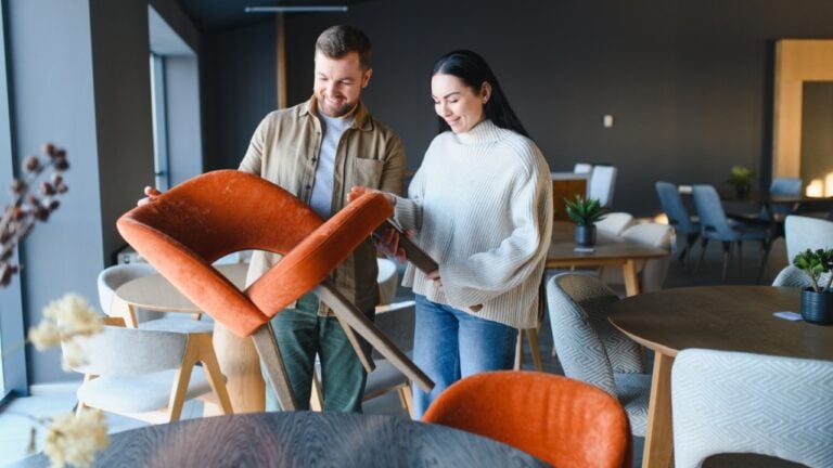Couple smiling, examining and choosing new modern upholstered chairs for their home in a contemporary furniture showroom