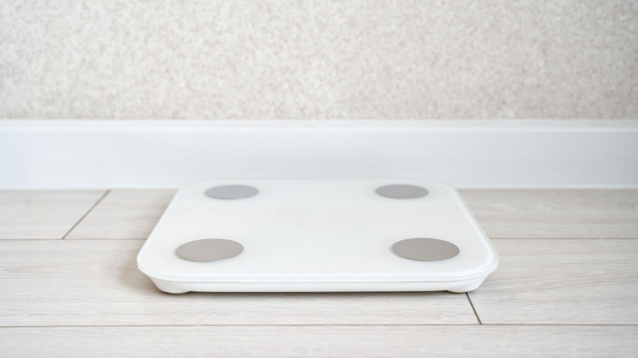 Digital bathroom scale on light wooden floor in minimalist room setting.