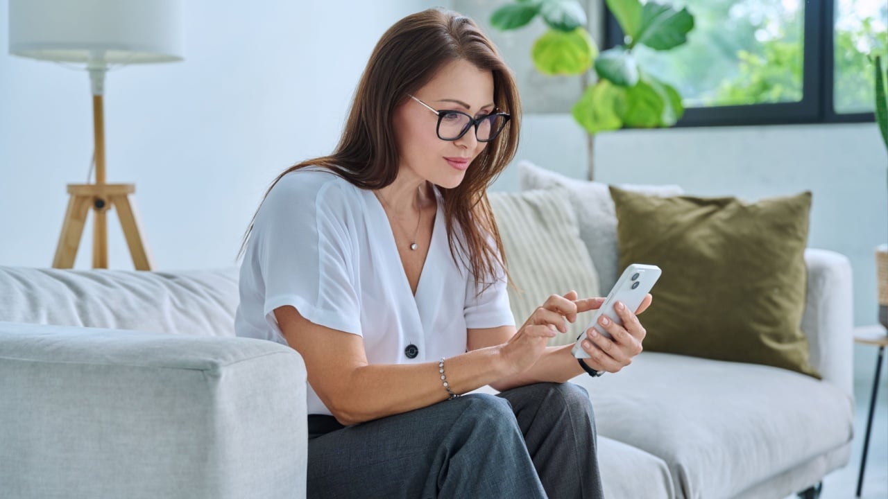 Middle aged relaxed woman on couch at home using smartphone
