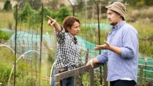 Female worker in jeans and checkered shirt is arguing with male neighbor of garden and country plot, querulous angry ranch owners. Customers and workers sort things out, shout and insult each other