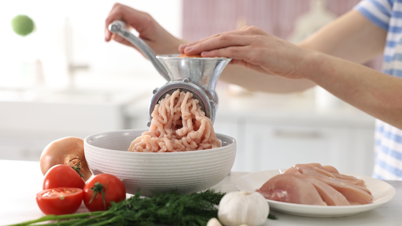 Woman making minced meat with grinder at white marble table in kitchen, closeup