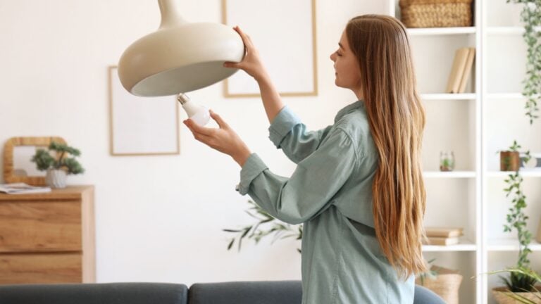 Young woman screwing light bulb into ceiling lamp at home
