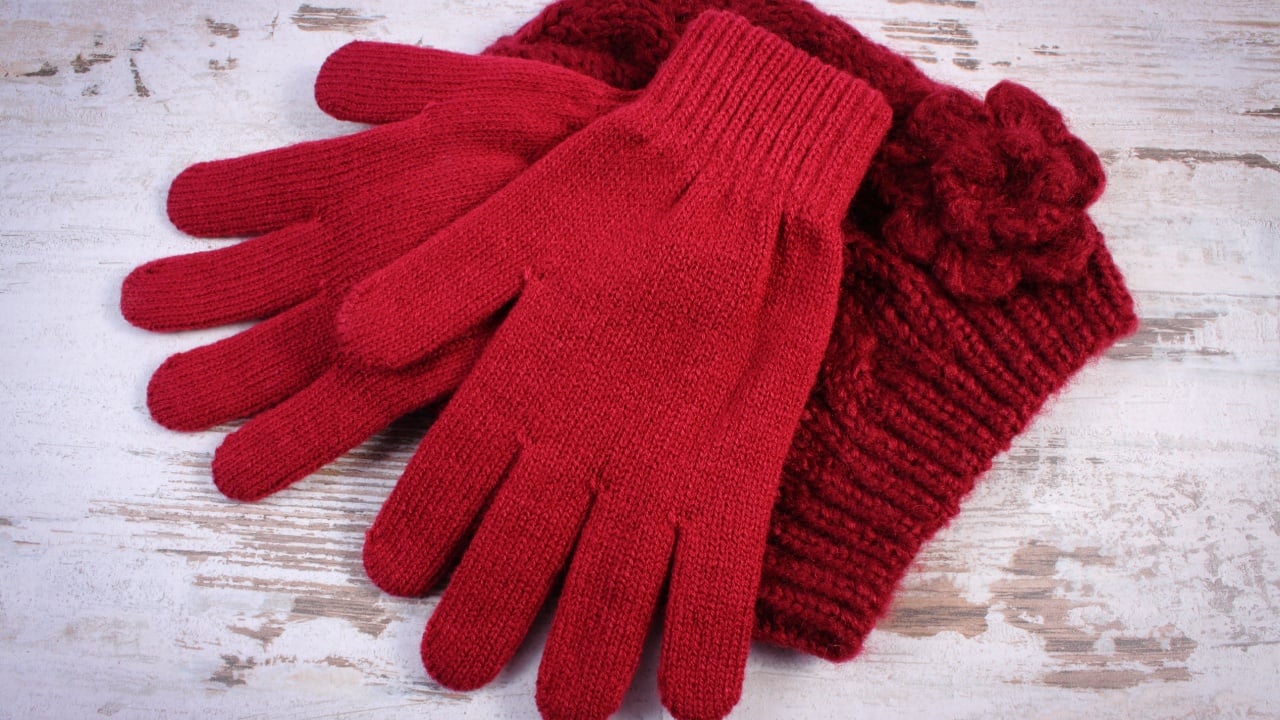 Pair of woolen gloves and cap for woman on old rustic wooden background, womanly accessories, warm clothing for winter, burgundy color