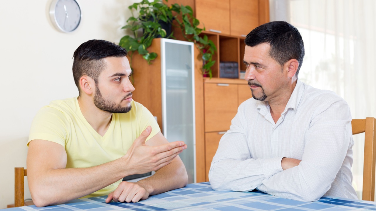 Domestic quarrel between mature father and adult son at the table in the living room