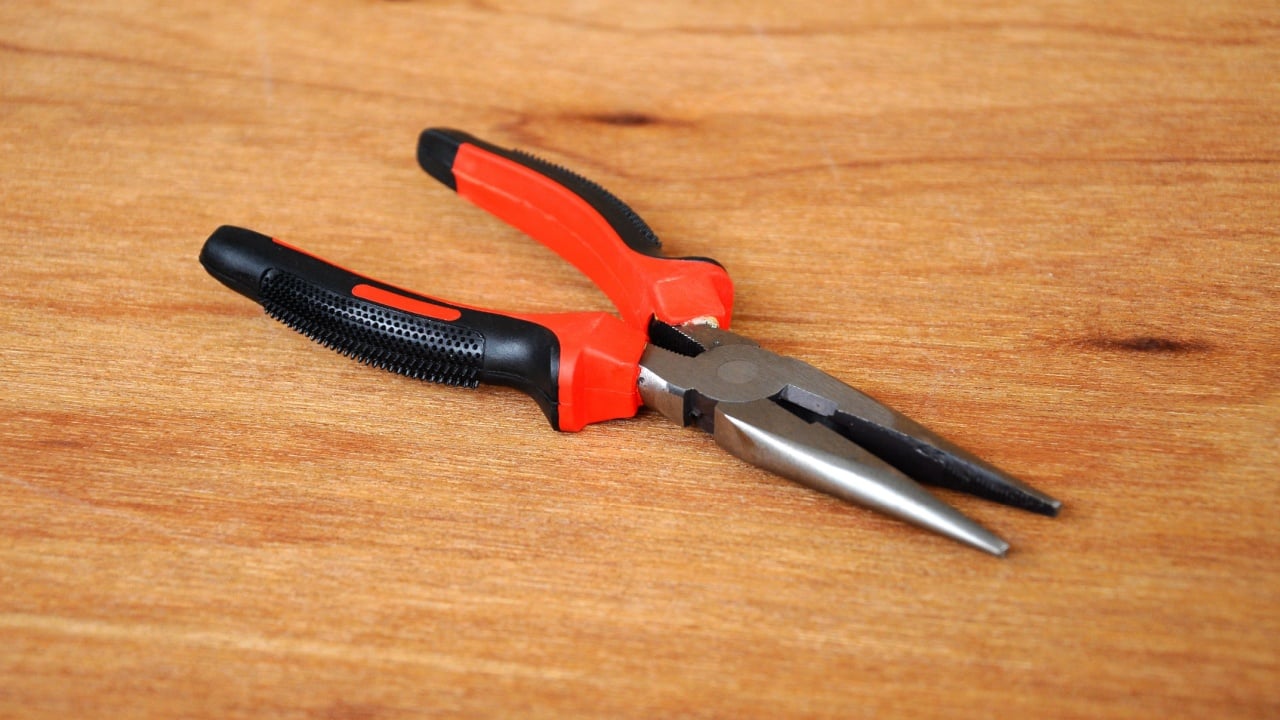 Needle Nose Pliers also known as pointy nose pliers or long nose pliers isolated on wood grain texture background.