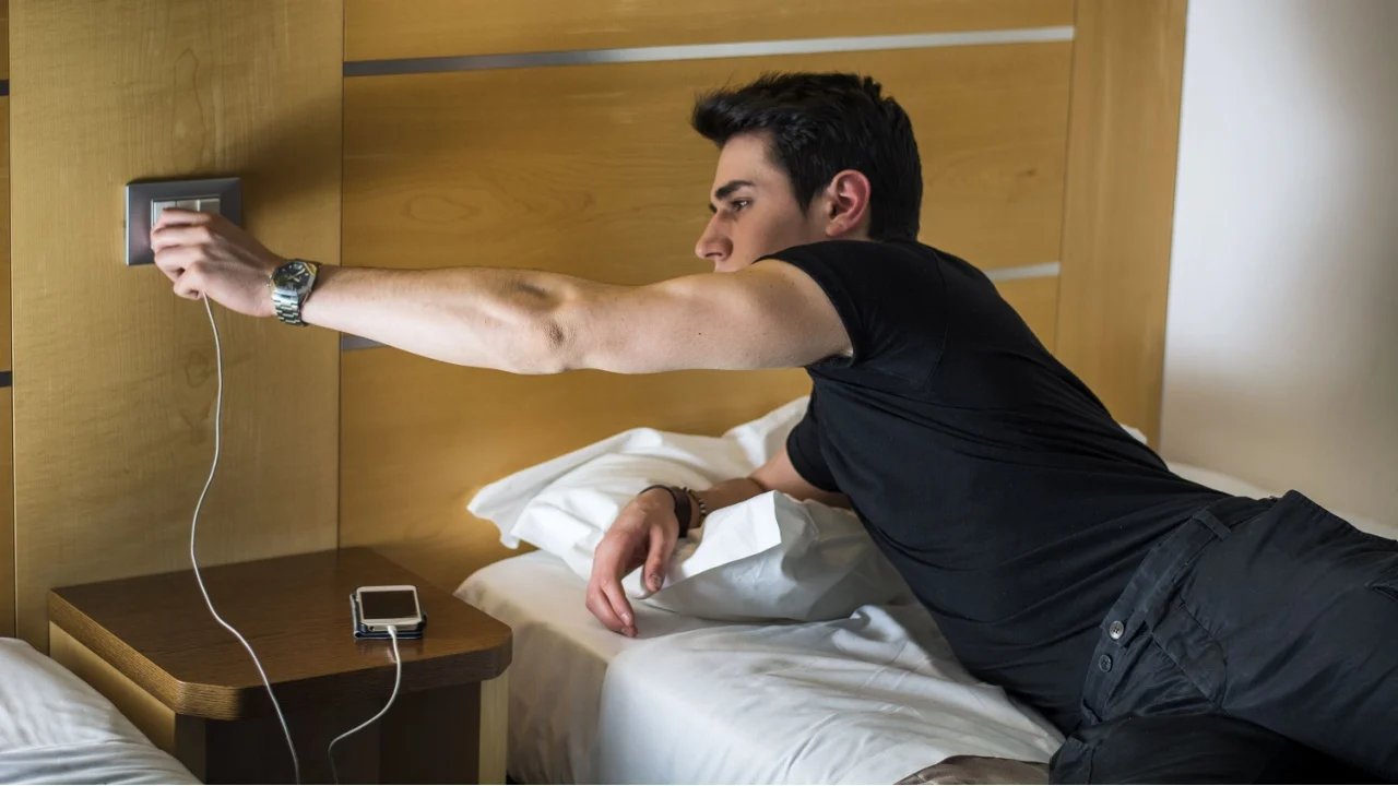 Serious Gorgeous Young Man Connect his Mobile Phone to a Charger While Lying on his Side on the Bed.