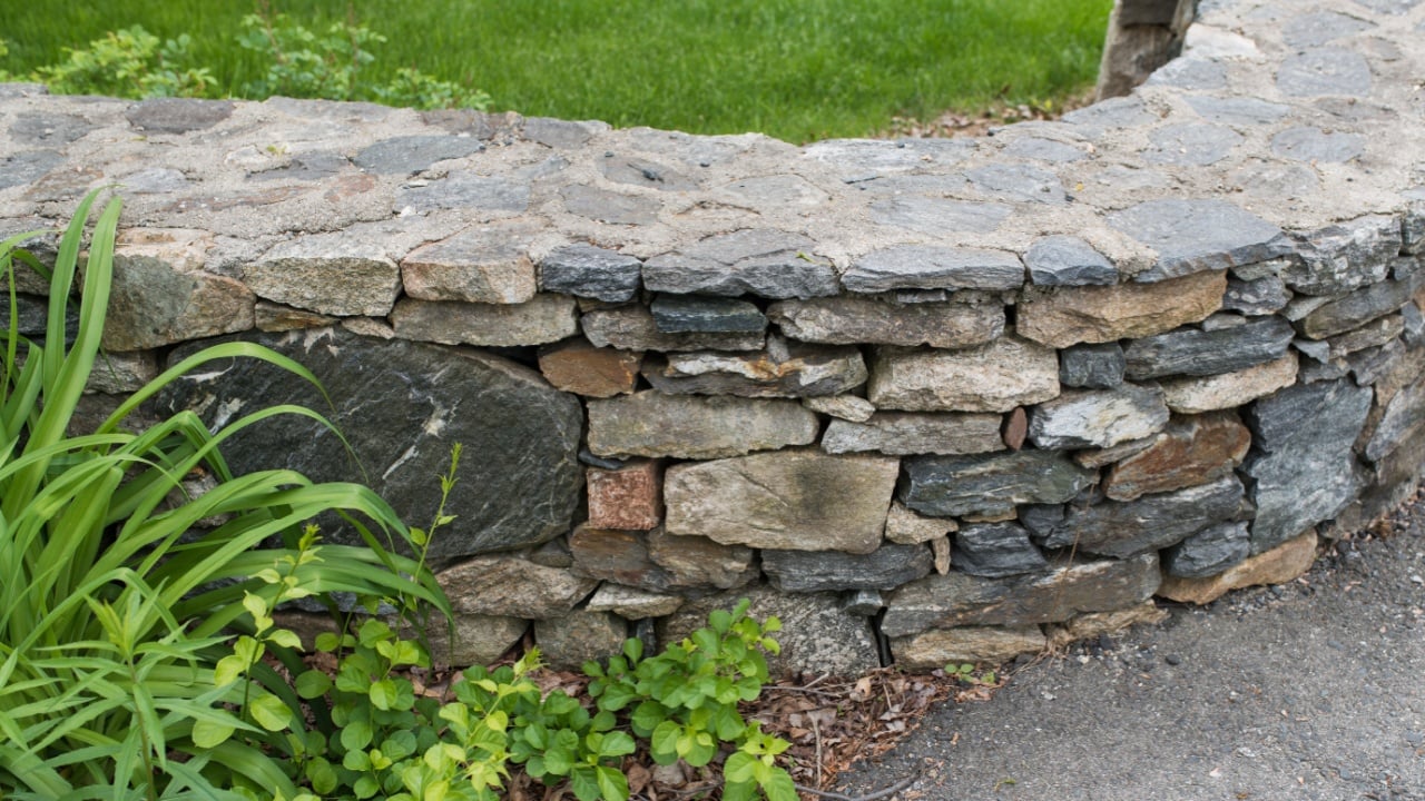 Siding and stone wall at the edge of residential neighborhood yard. Landscape and yard care background.