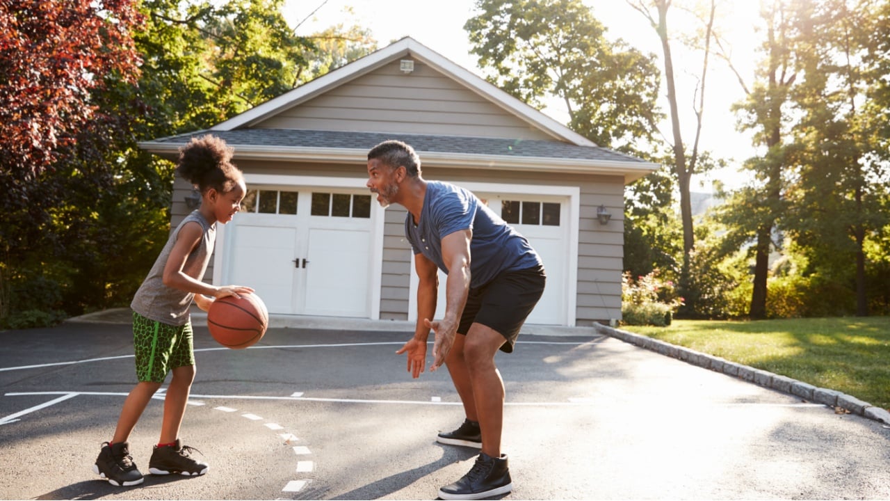 Father And Son Playing Basketball On Driveway At Home