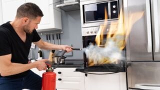 Man Using Fire Extinguisher To Put Out Fire From Oven At Home