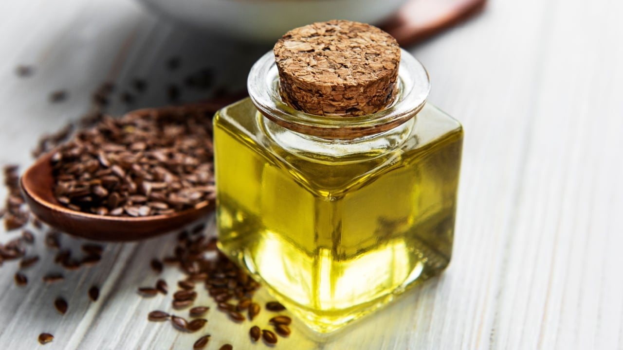 Flax seeds or linseeds in spoon and bowl with glass of linseed oil on wooden backdrop