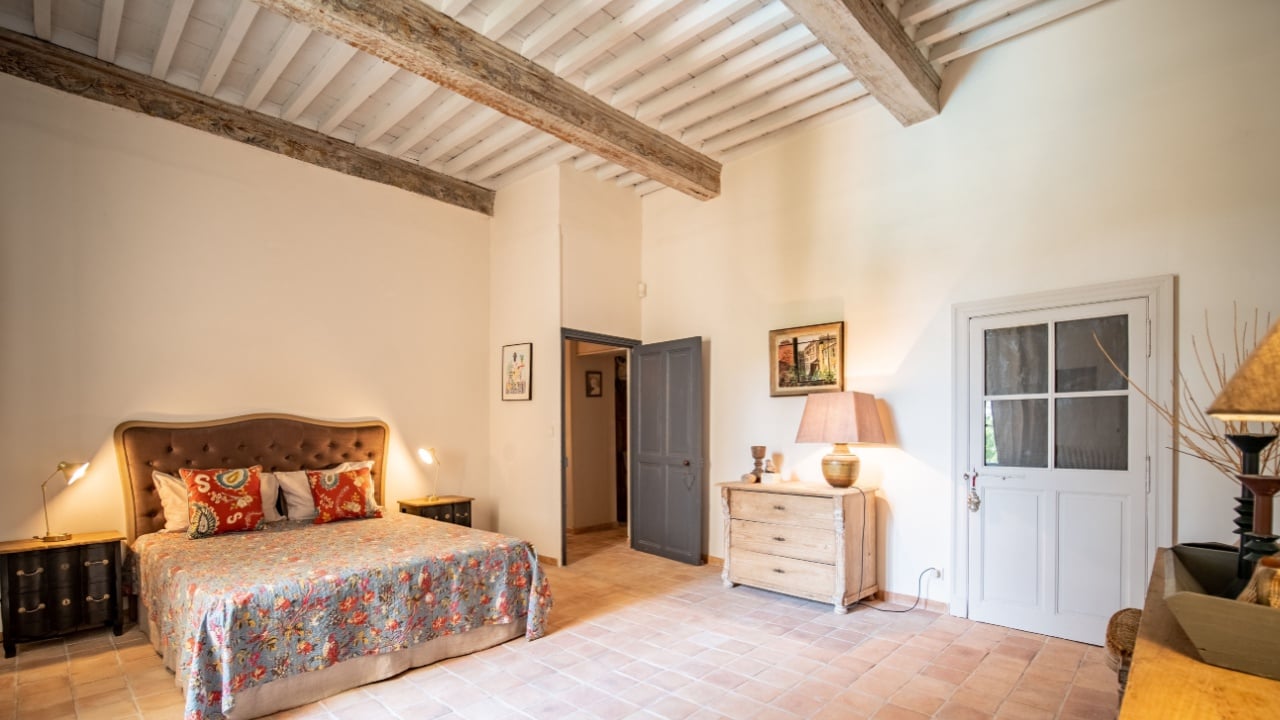 Ales, France - June 16th 2022 : large spacious vintage room with bedside tables, vintage bed, brick floor, white walls, grey and white door, wooden table on the right