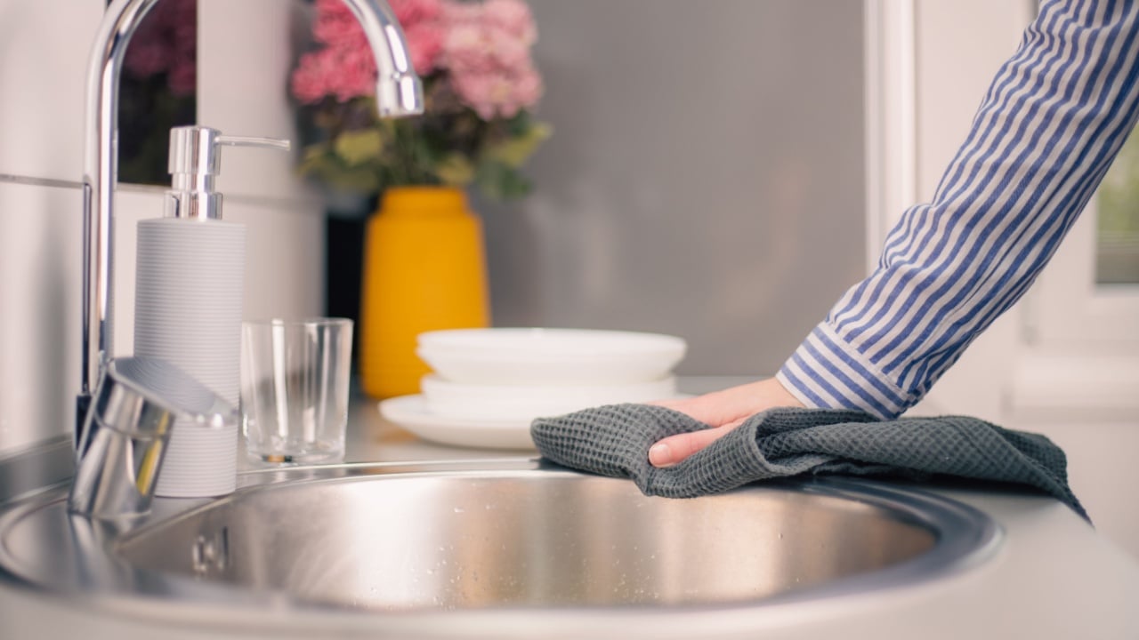 Hand of woman cleaning the kitchen counter and sink after washing dishes. Housewife doing housework concept.