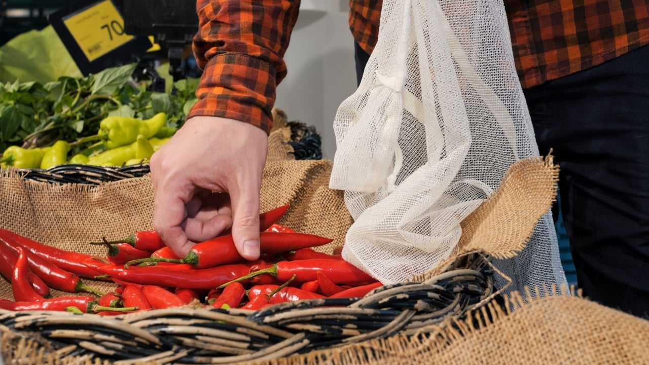 Cinematic footage, buying chili peppers at vegetable market. Man puts red chili peppers in reusable bag for cooking spicy dishes. Lovers of spicy dishes with high content of hot peppers. Burning chili