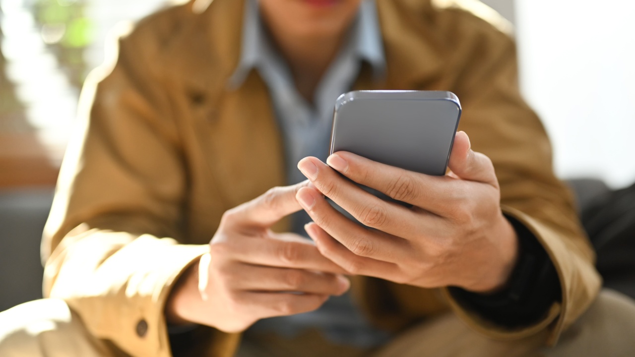 Selective focused on hands. Man chatting online in social network on smart phone while sitting on couch at home
