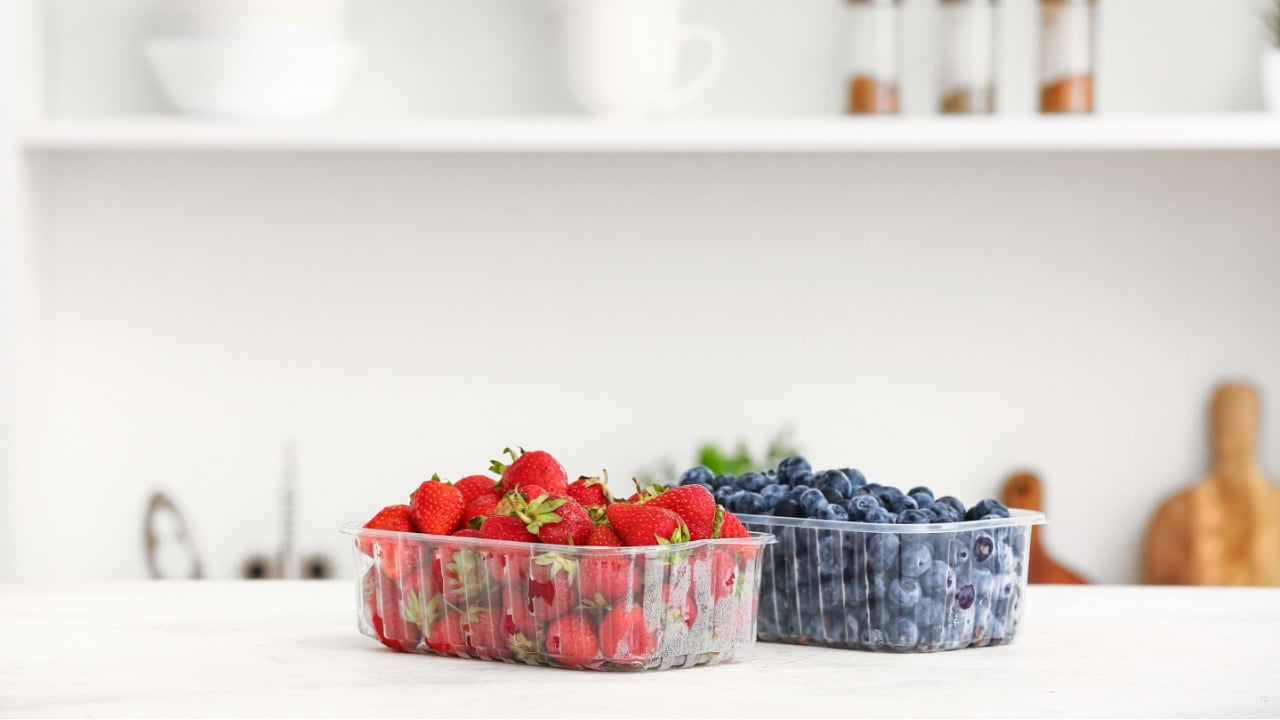 Plastic containers with ripe berries on table in kitchen