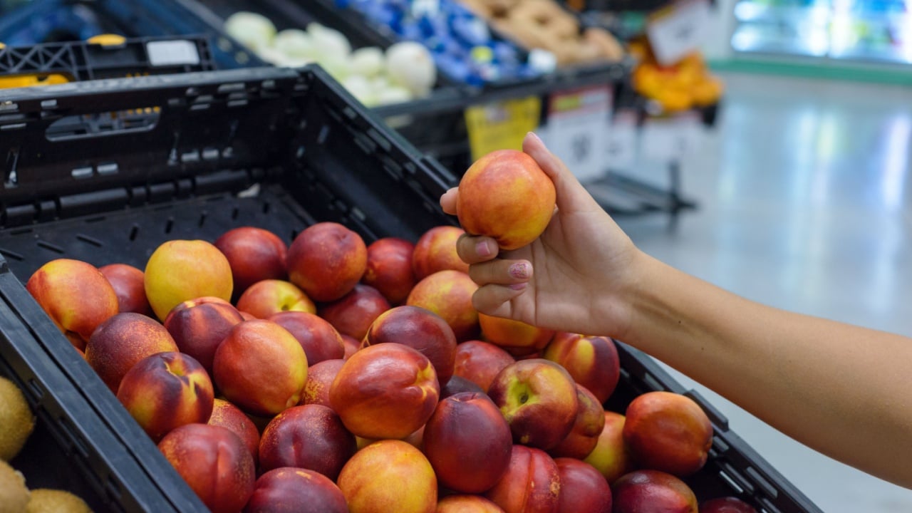 Hand holding a nectarine in a supermarket.