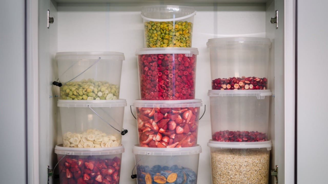 a pantry shelf stocked with clear, stackable containers filled with various dried fruits and grains.