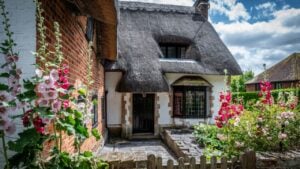 Cottage garden with hollyhocks in front of a picturesque thatched cottage in Wherwell, Hampshire, England on 4 July 2024